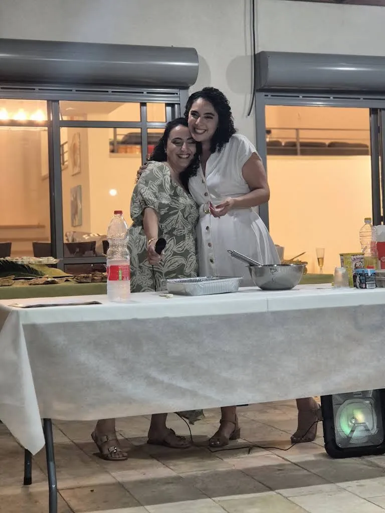 שתי נשים מחובקות ומחייכות ליד שולחן באירוע